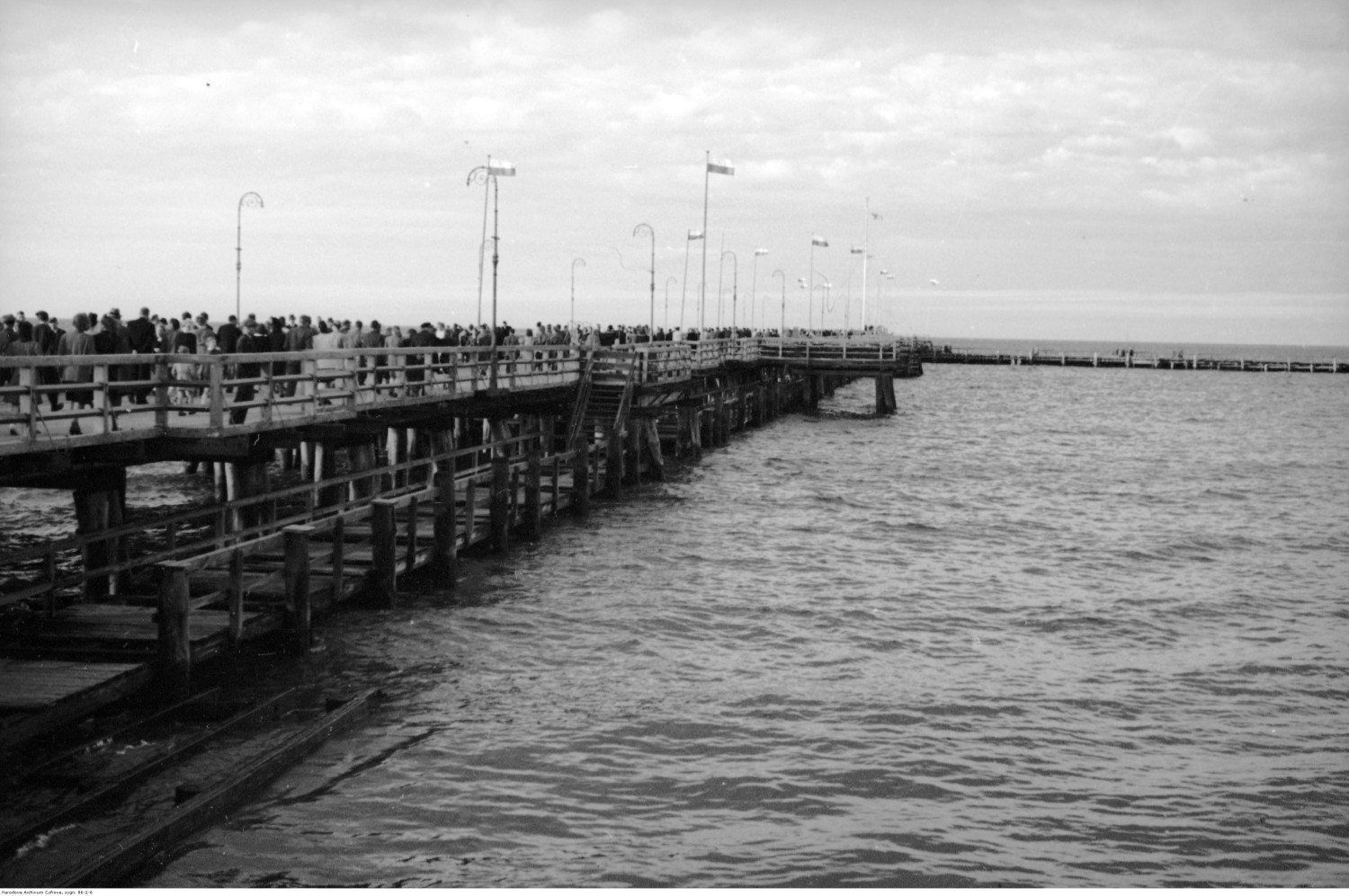 Molo - widok ogólny. Widoczne flagi państwowe i spacerujący ludzie. Fot. Narodowe Archiwum Cyfrowe.